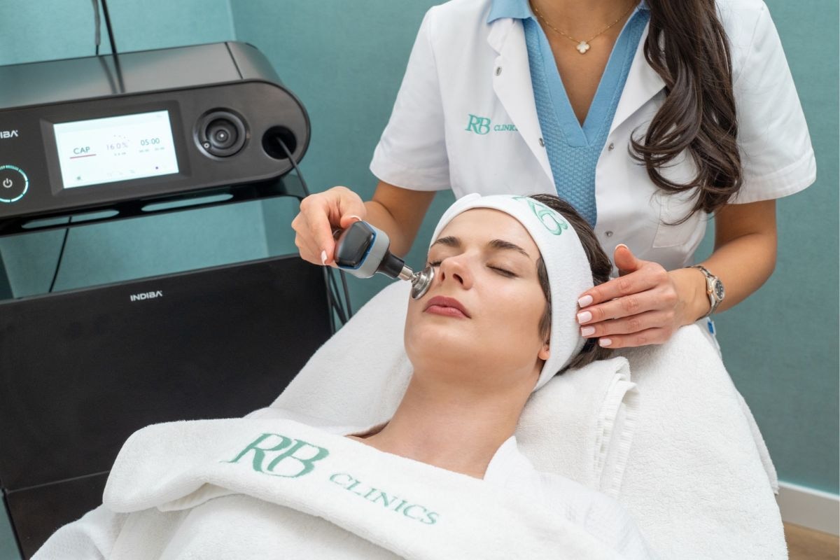 Specialist van RB Clinics behandelt het gezicht van een cliënte met de Indiba Edna Pro Max op de achtergrond